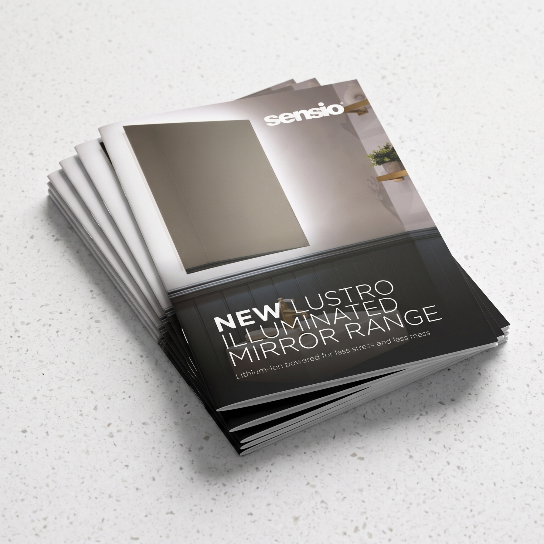 A stack of Sensio brand glossy mirror catalogs or brochures displayed on a light speckled countertop. The cover features a large reflective mirror sample and white text reading 'NEW LUSTRO ILLUMINATED MIRROR RANGE'.