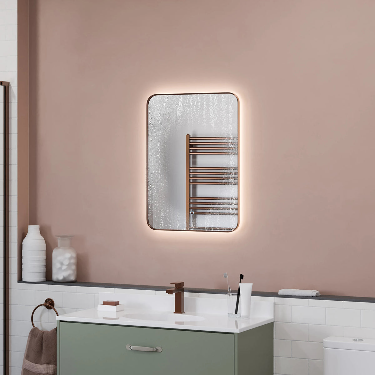 A rectangular wall-mounted mirror with a warm white LED light border, shown in a styled bathroom setting above a vanity with a green cabinet and white tiles. #Finish_Bronze
