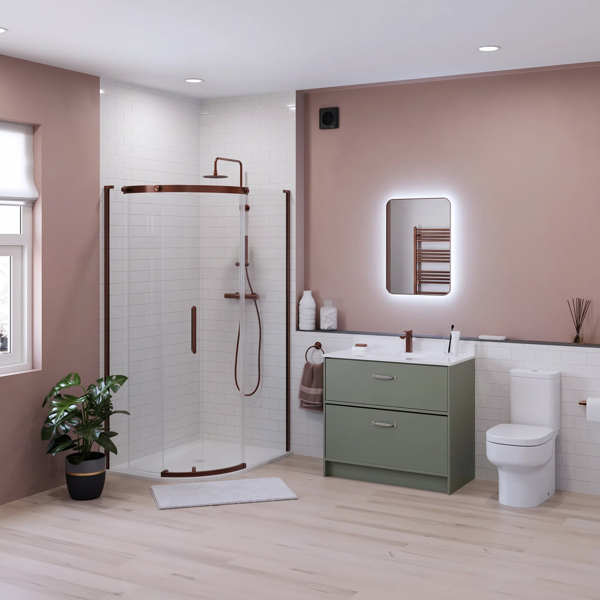 A modern bathroom interior featuring a green two-drawer vanity with a white sink, a white toilet, a glass shower enclosure with bronze hardware, and a pink accent wall with a built-in lighted mirror. #Finish_Bronze